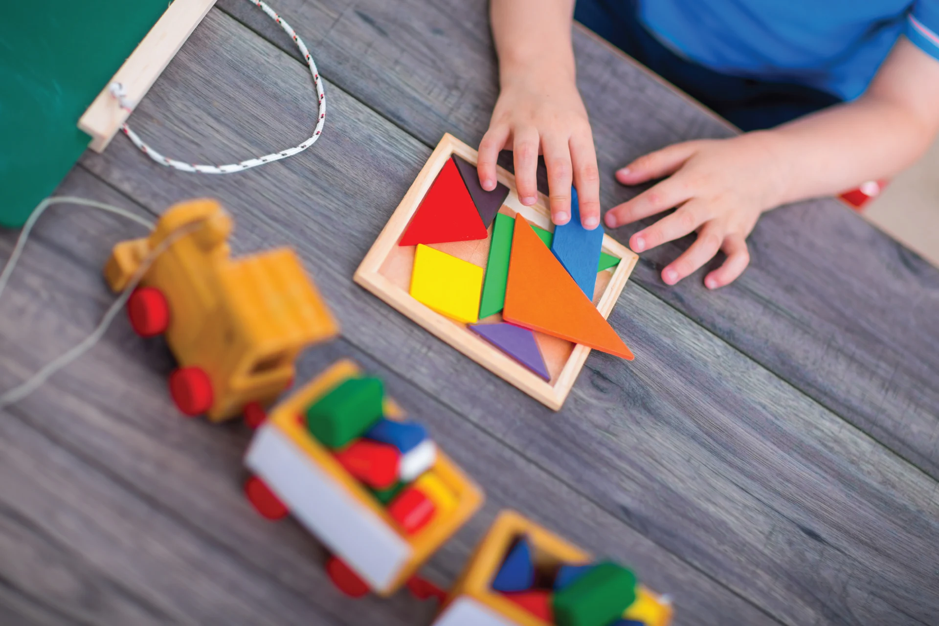 Child assembling colored geometric shapes on a wooden table.