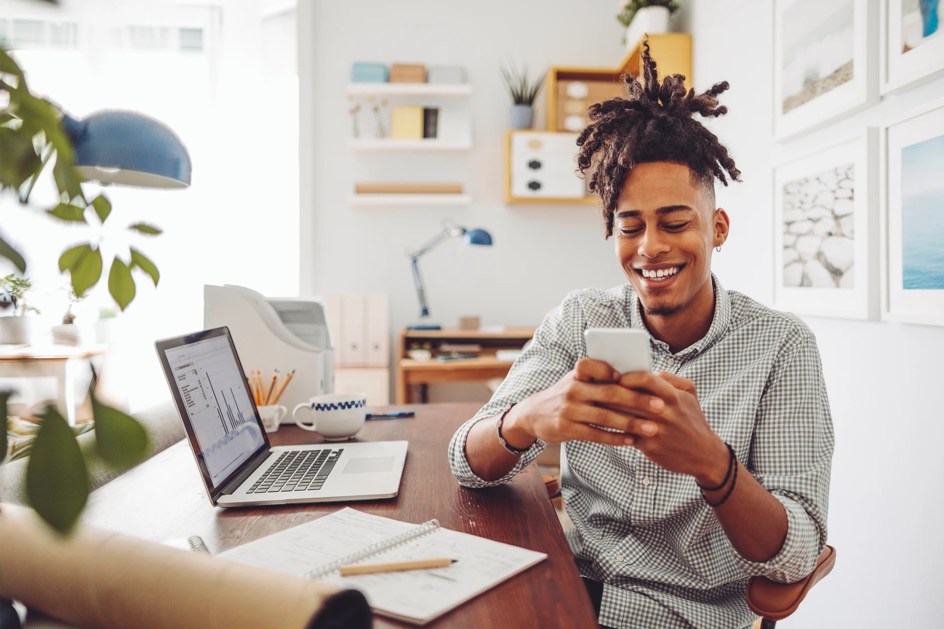 Person using a smartphone while sitting at a desk with a laptop.