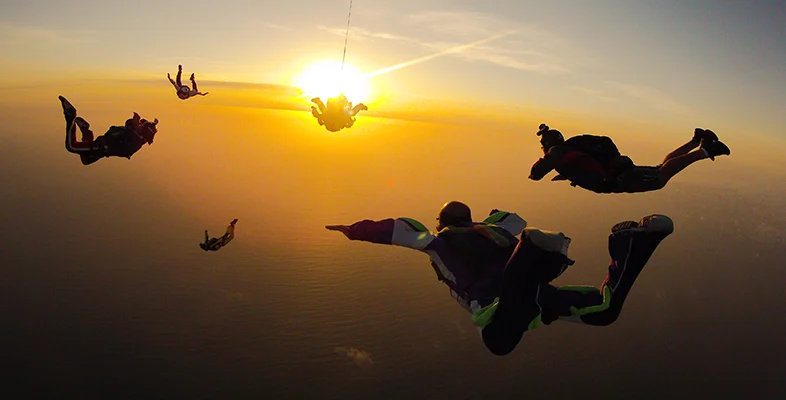 Group of skydivers performing freefall jump dive towards ocean sunset