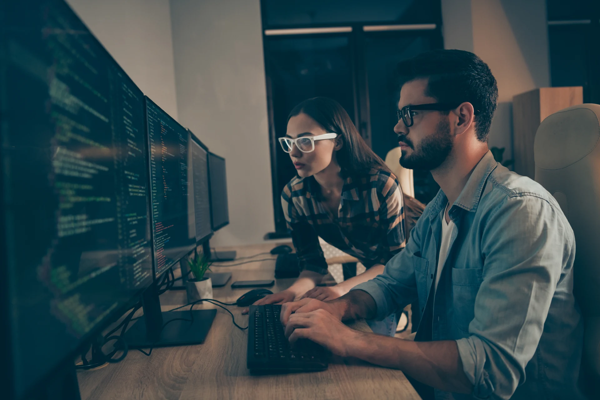 Two professionals collaborating at a computer with programming code.
