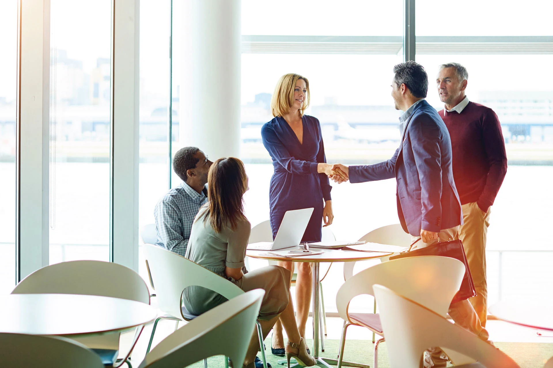 Two professionals shaking hands while others observe in a meeting.