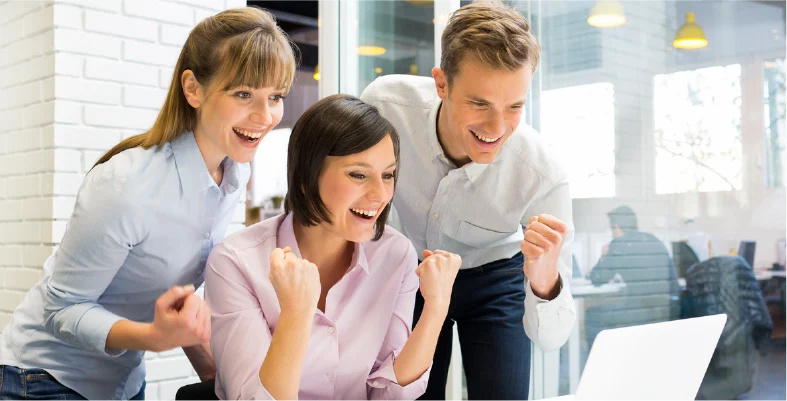 Three corporate colleagues high fiving and celebrating success inside office