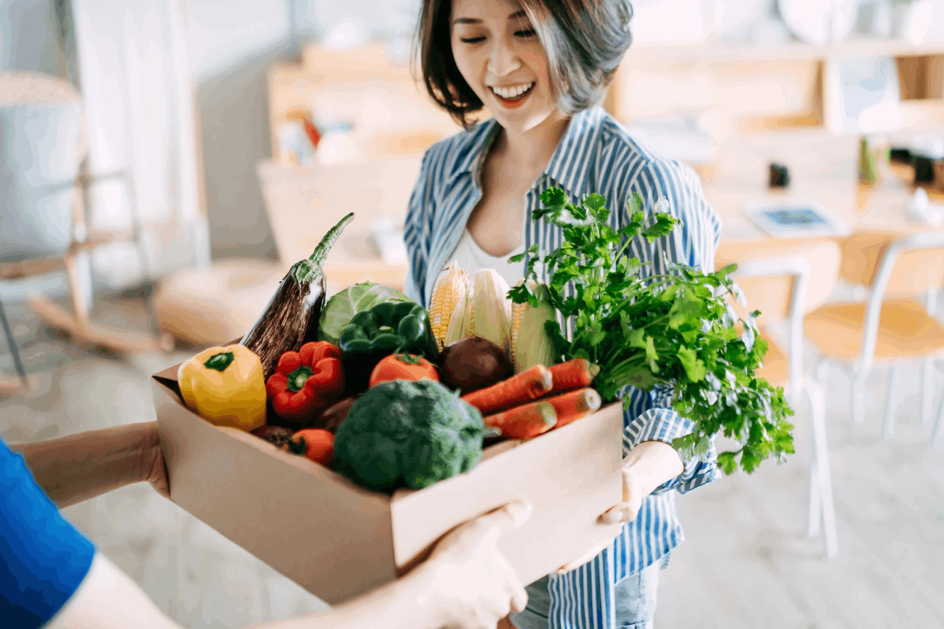 Person delivering a box of fresh vegetables in a home setting.