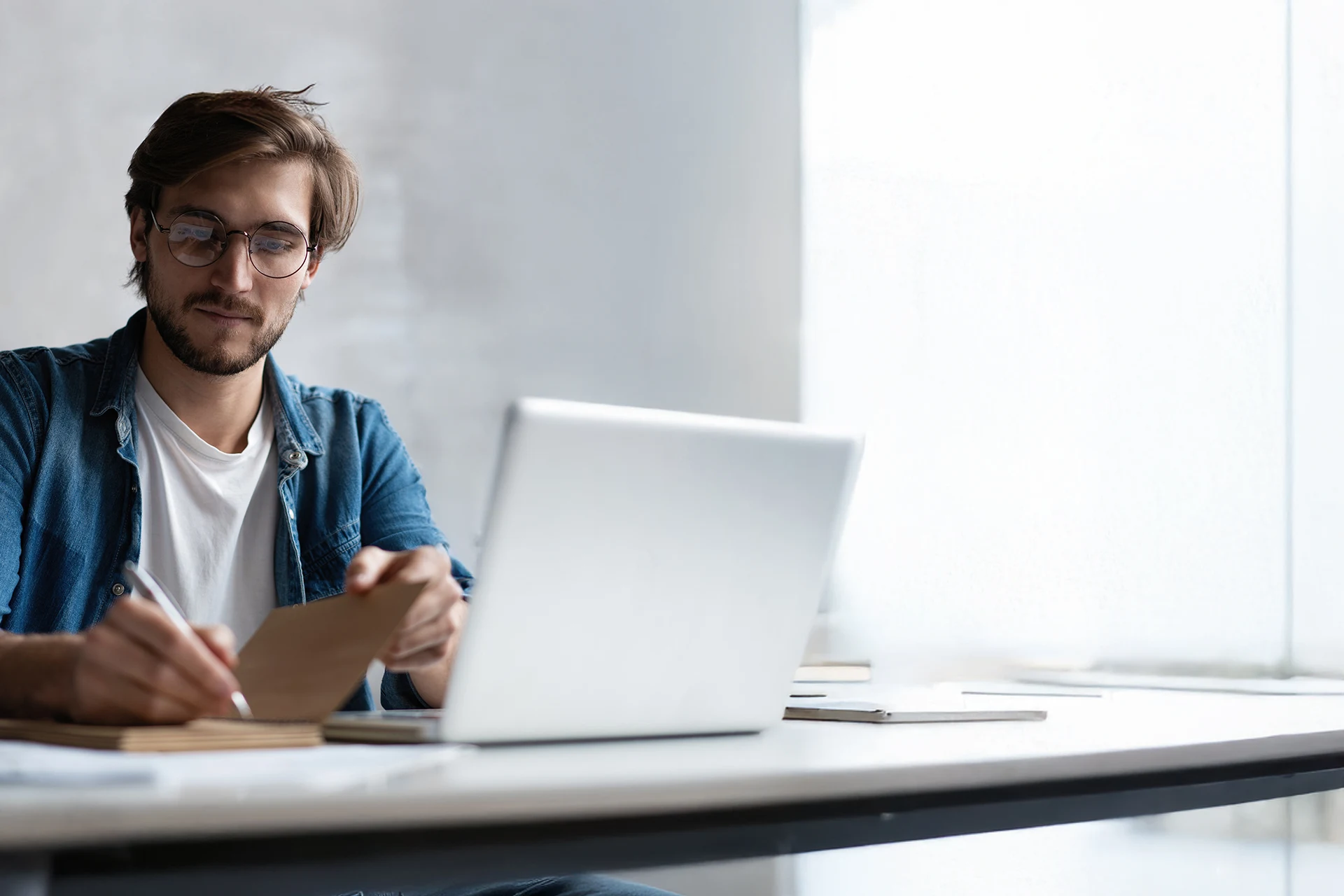 Individual writing notes while working on a laptop in a modern setting.