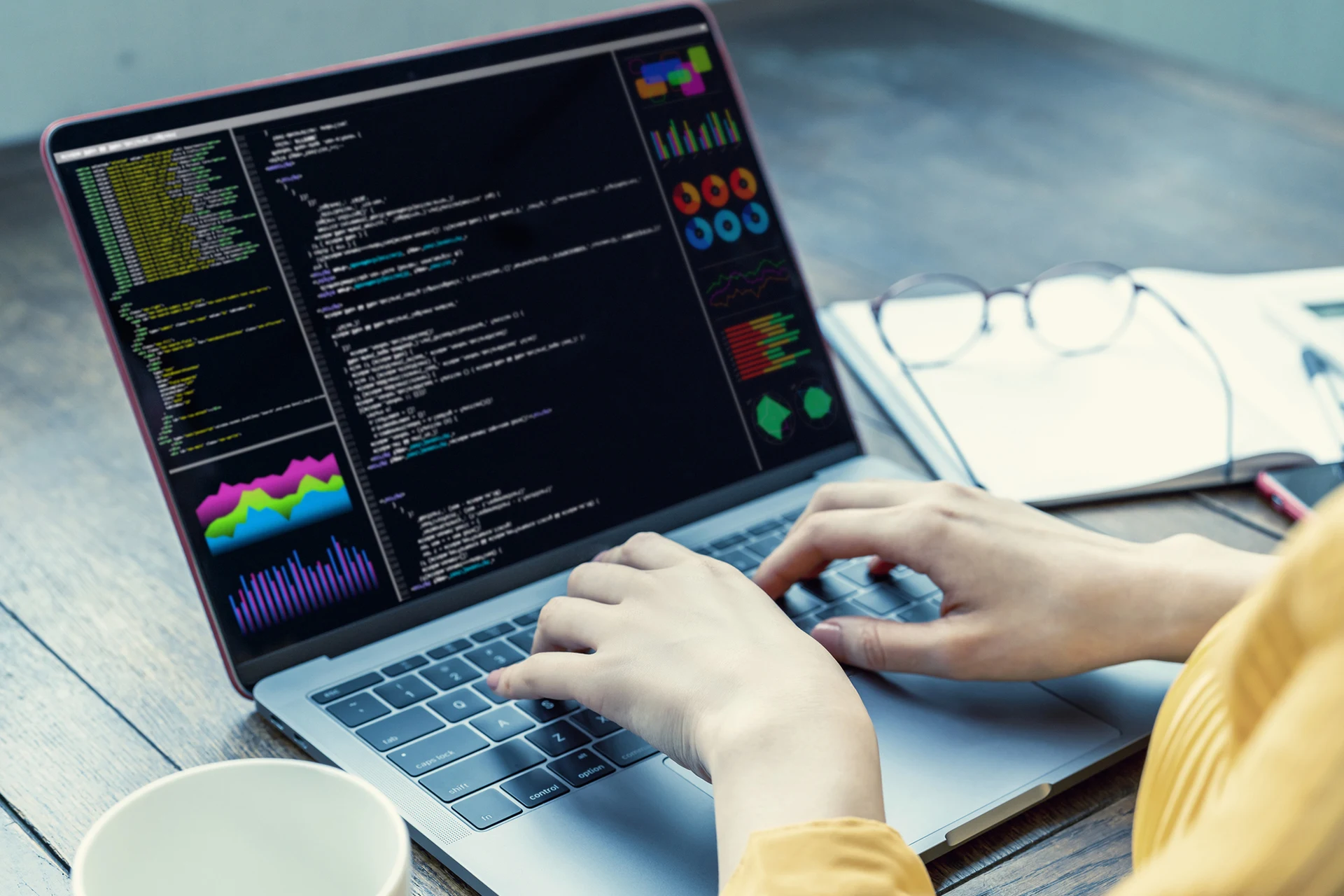 Person typing on a laptop displaying code and data visualizations.