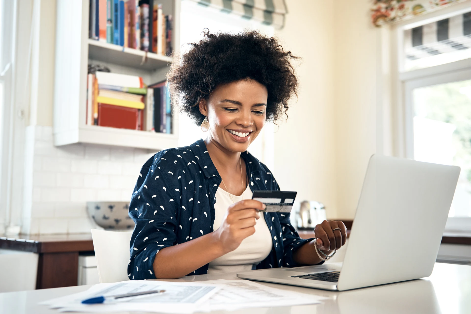 Person using a laptop and holding a credit card at a workspace.