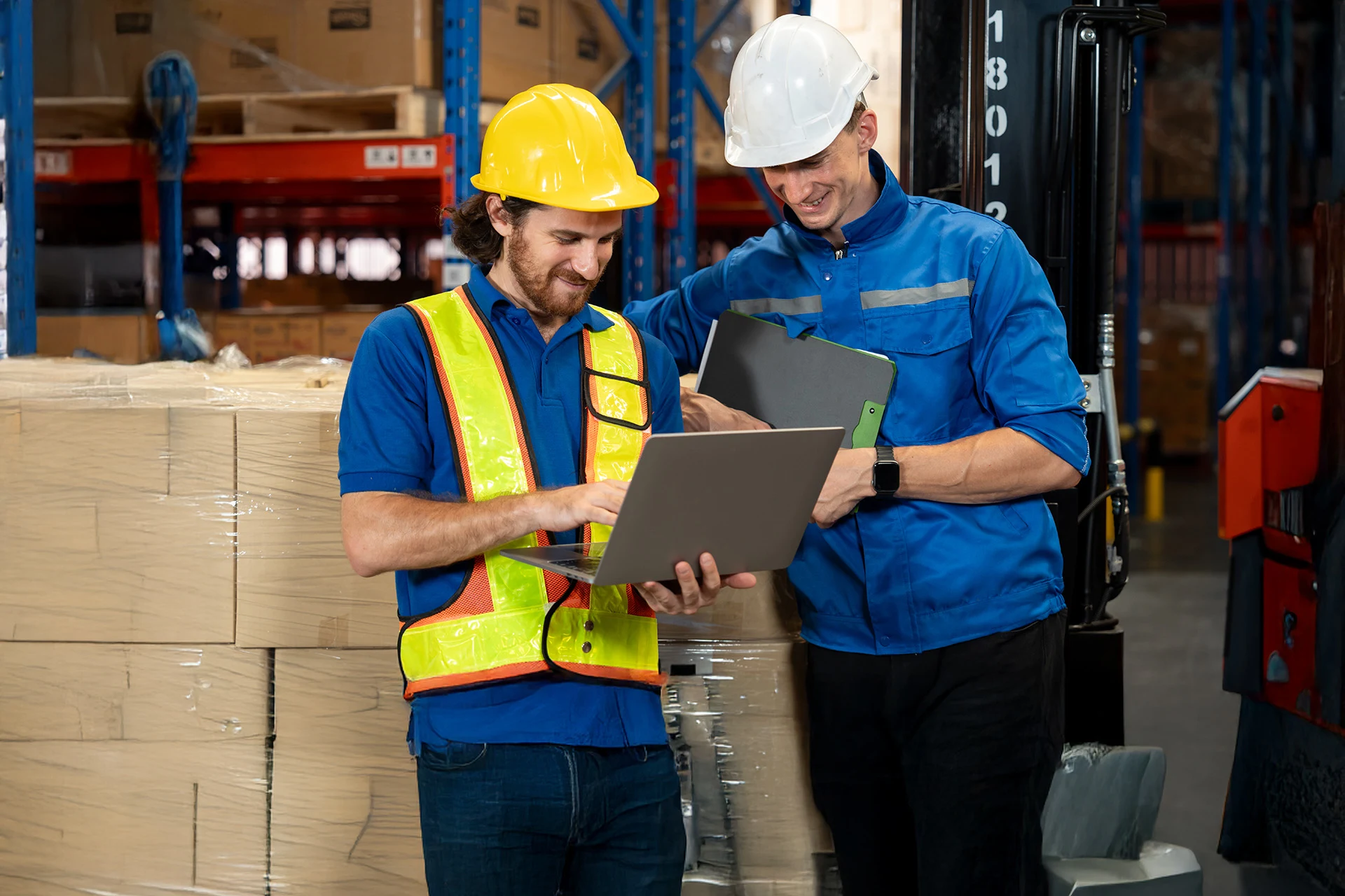 Two warehouse workers collaborating over a laptop in a storage area.