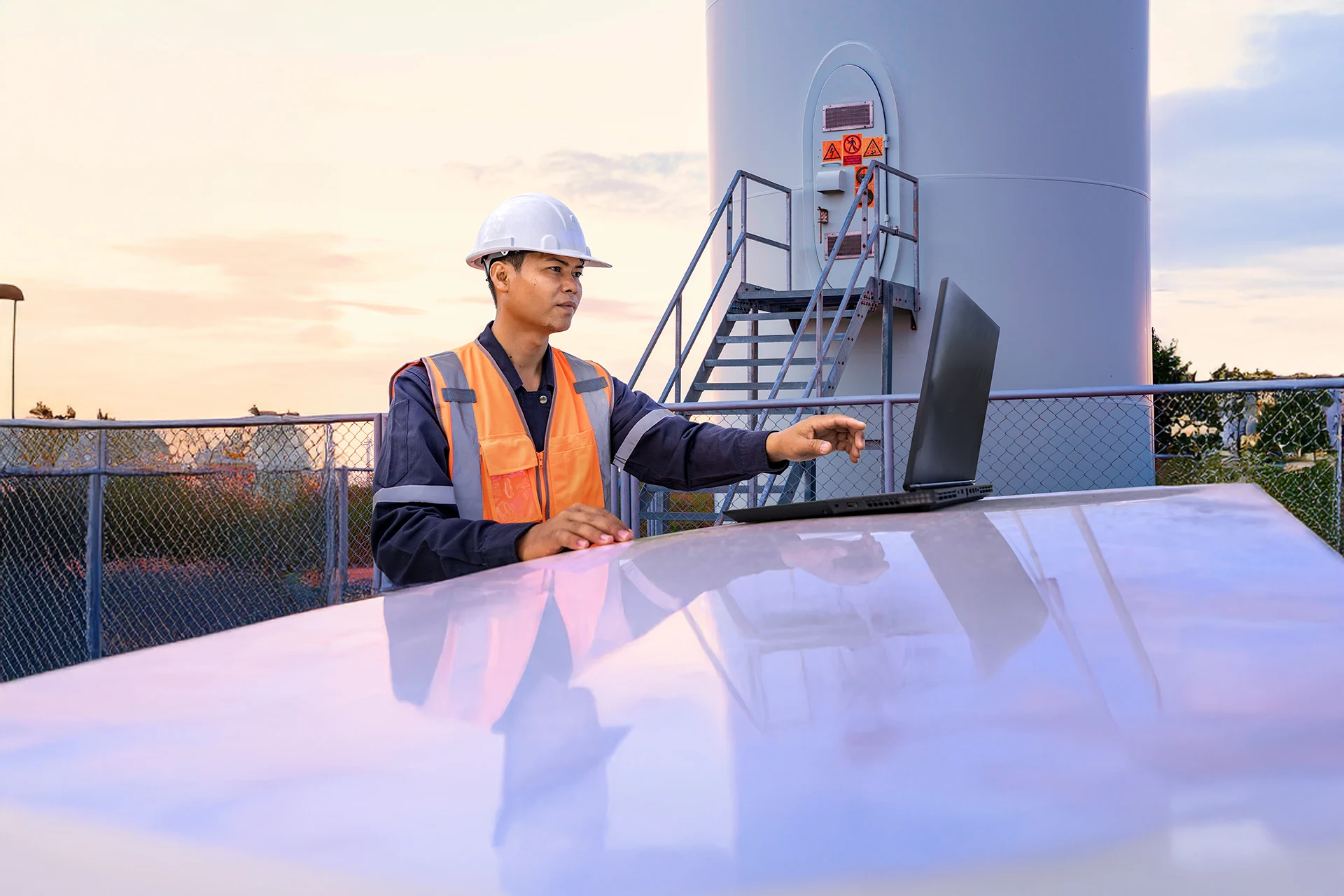 Technician using a laptop to monitor telecom equipment outdoors
