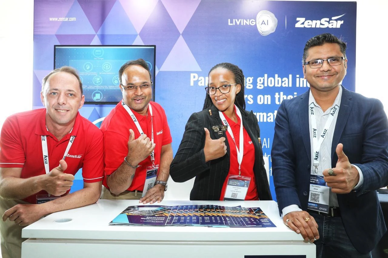 Four professionals posing thumbs up at Micro Focus Universe South Africa booth