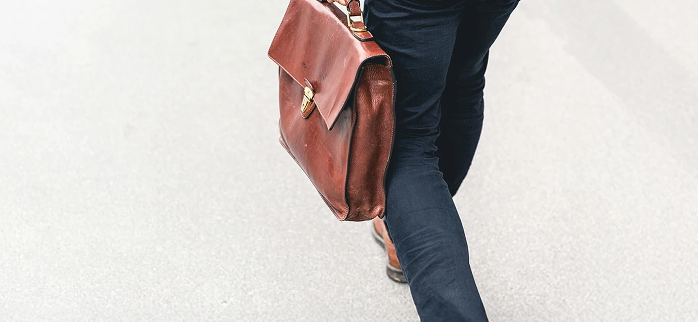 Professional walking through a modern corporate office with a leather bag