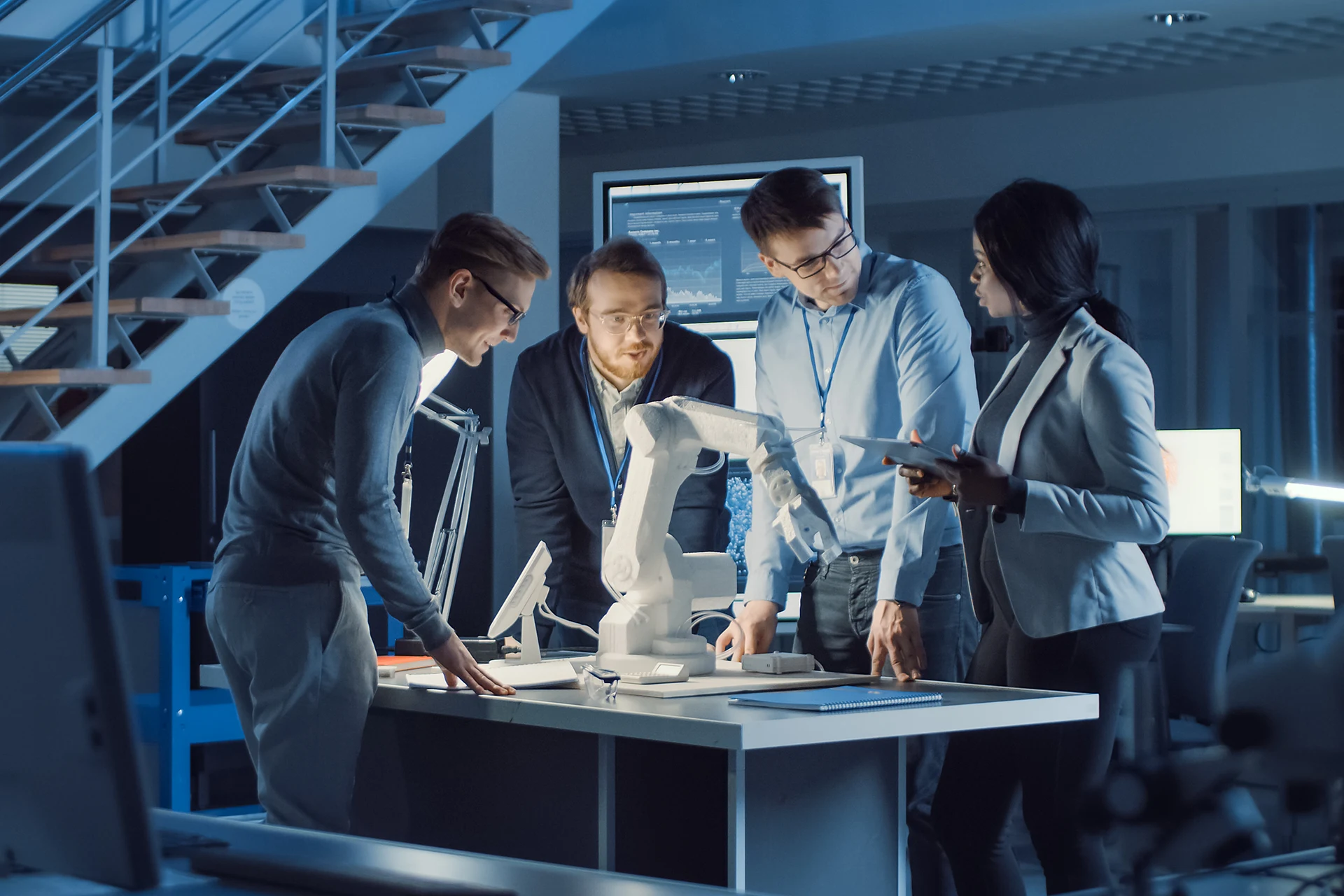 Team collaborating at a table with a robotic arm and tablets in a tech setting.
