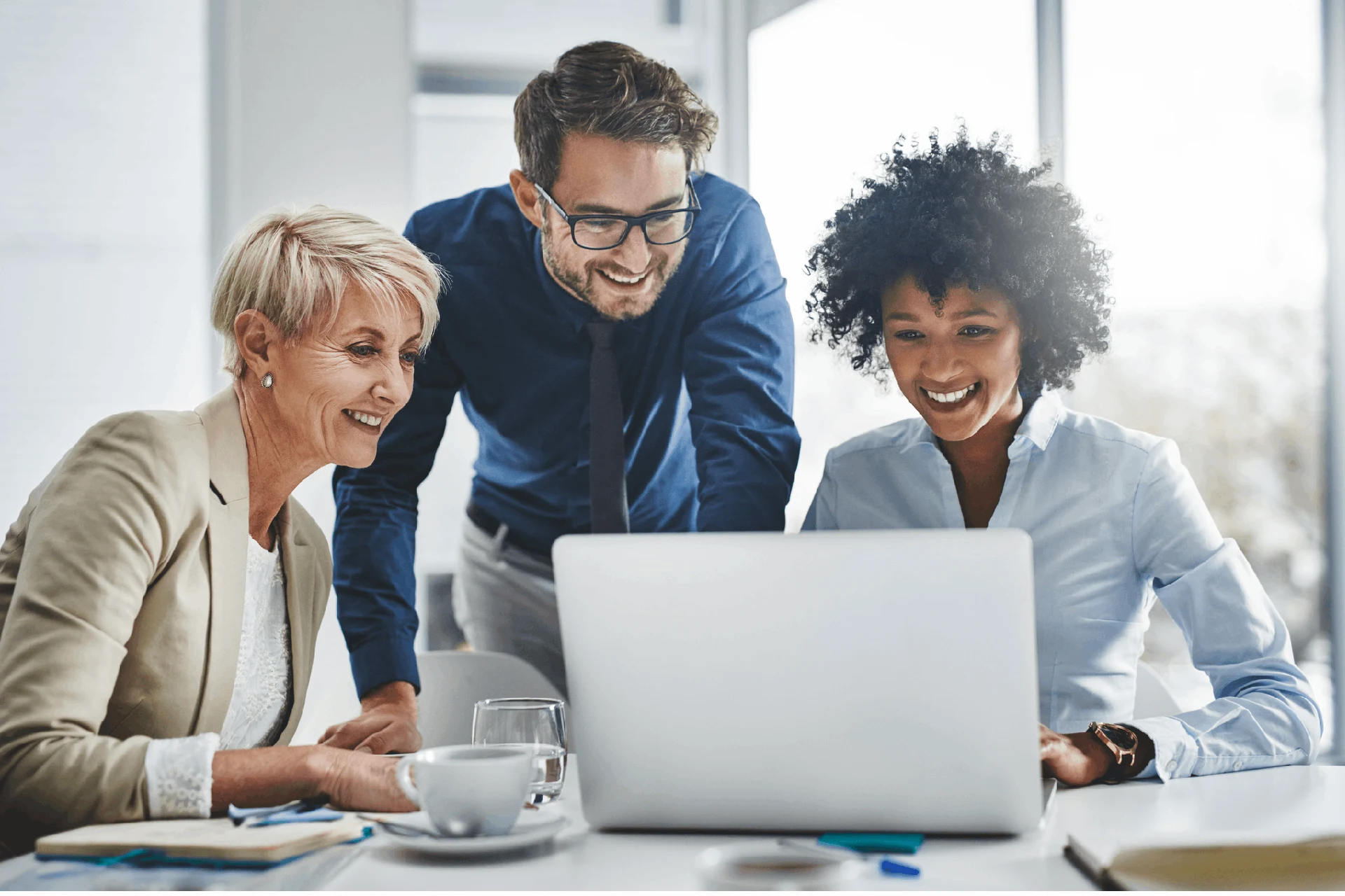 Three professionals collaborating over a laptop in a workplace setting.