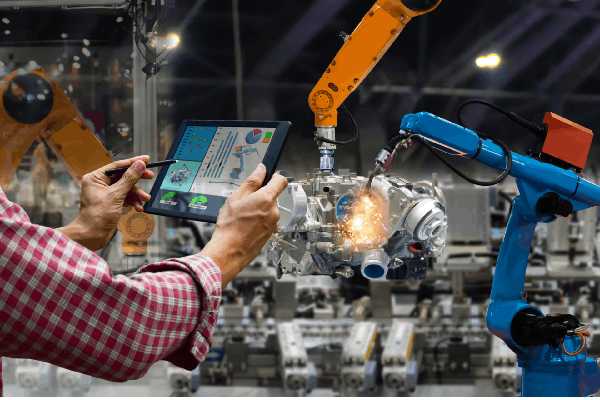 A worker using a tablet to monitor robotic arms in a manufacturing setup.