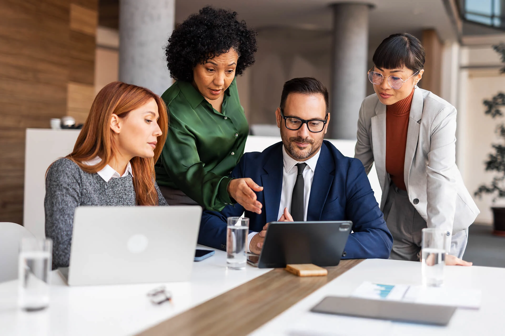 Four professionals collaborating over a tablet in an office setting