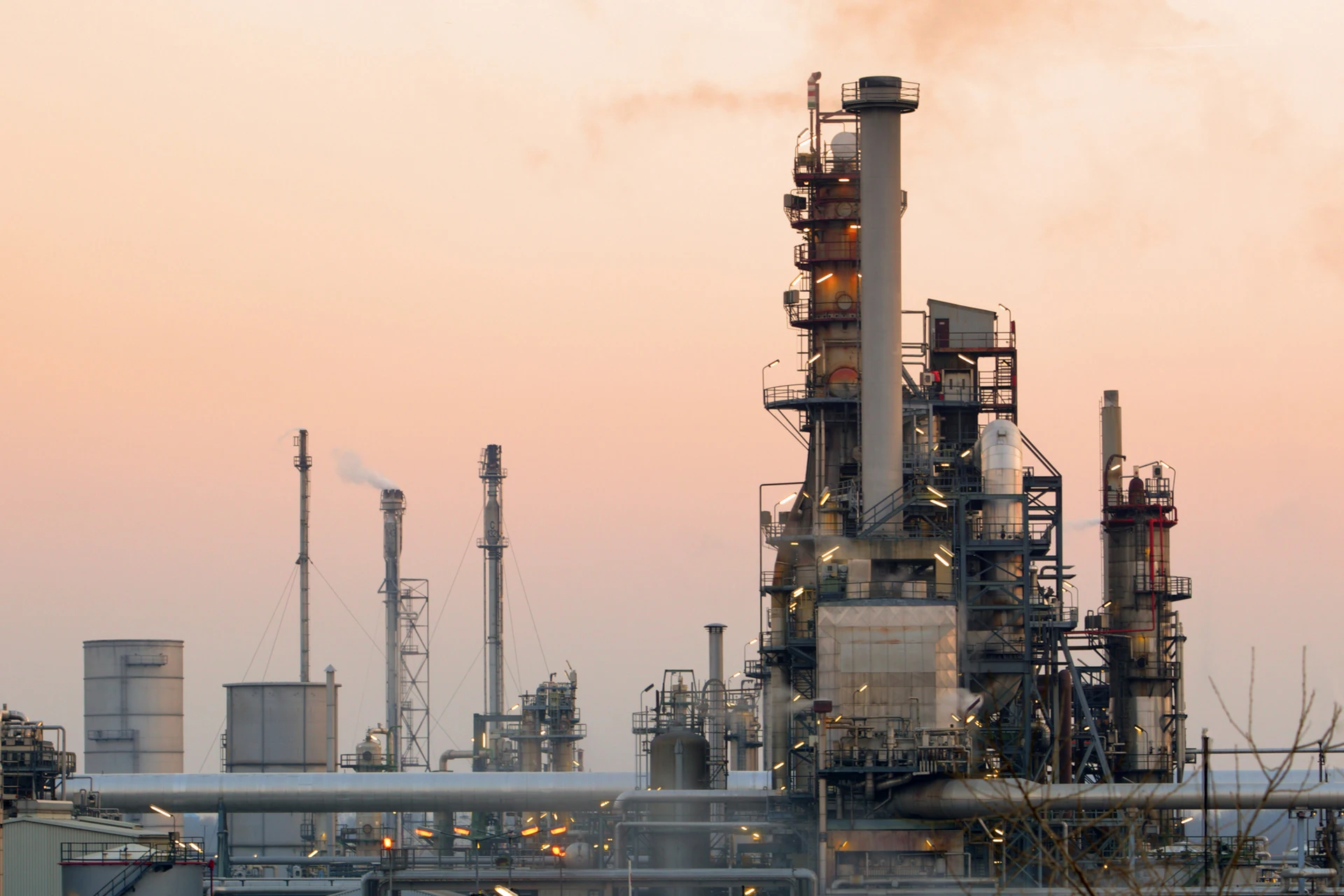 Industrial facility with smokestacks and pipelines at sunset