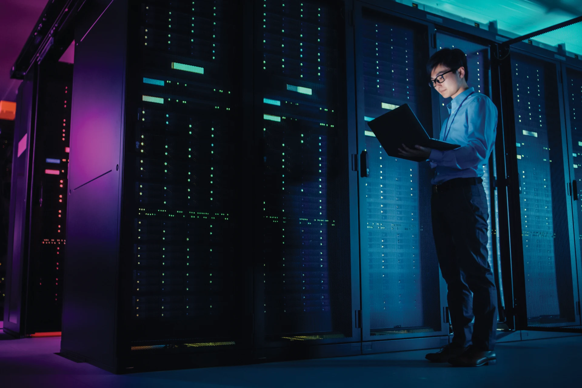 Professional reviewing data on a laptop in a server room environment.