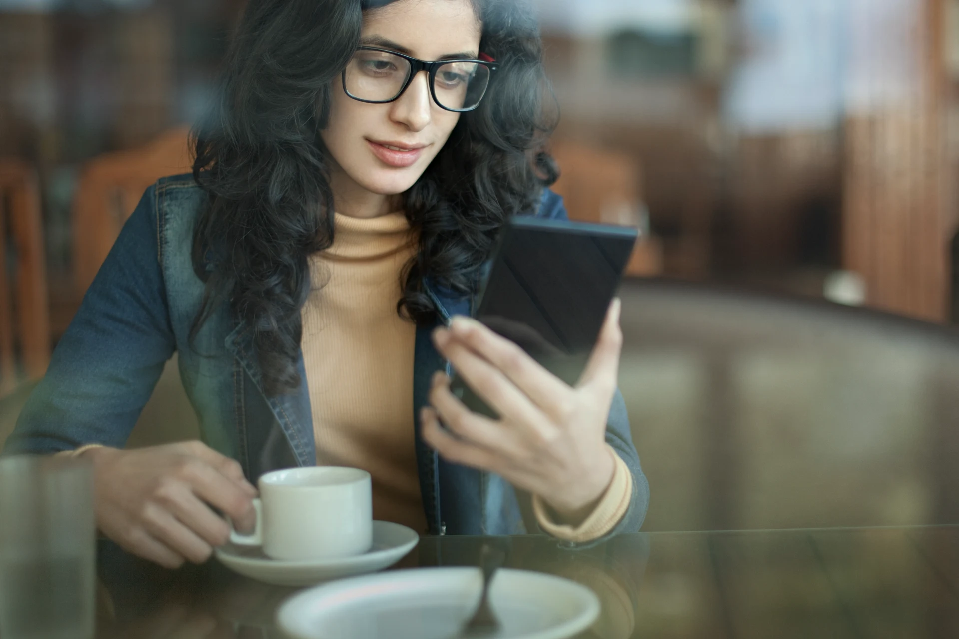 Woman sitting at a cafe, holding a smartphone while sipping coffee.