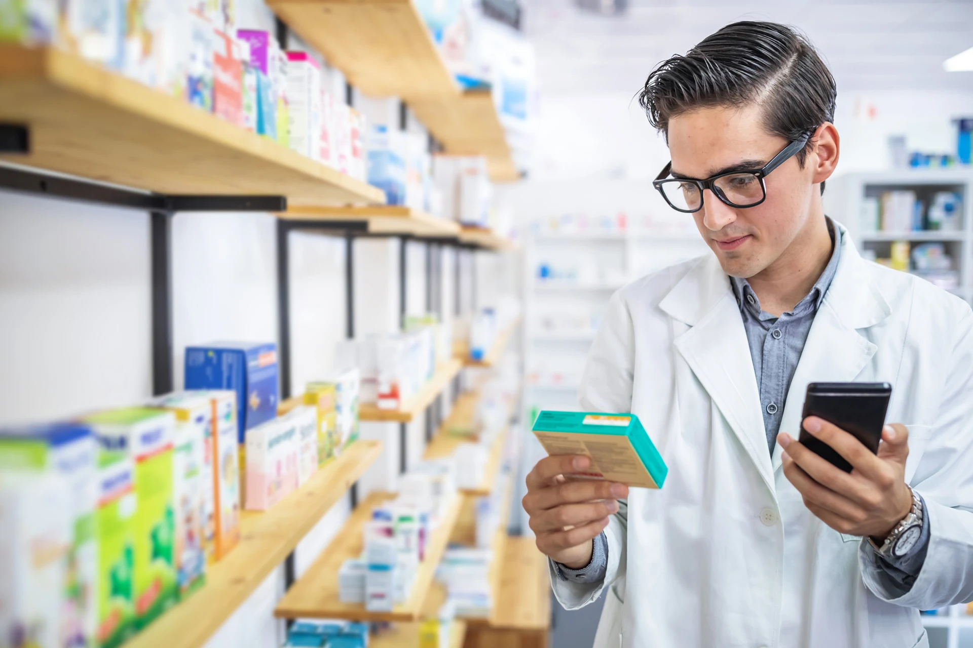 Pharmacist examining a medicine box while holding a smartphone