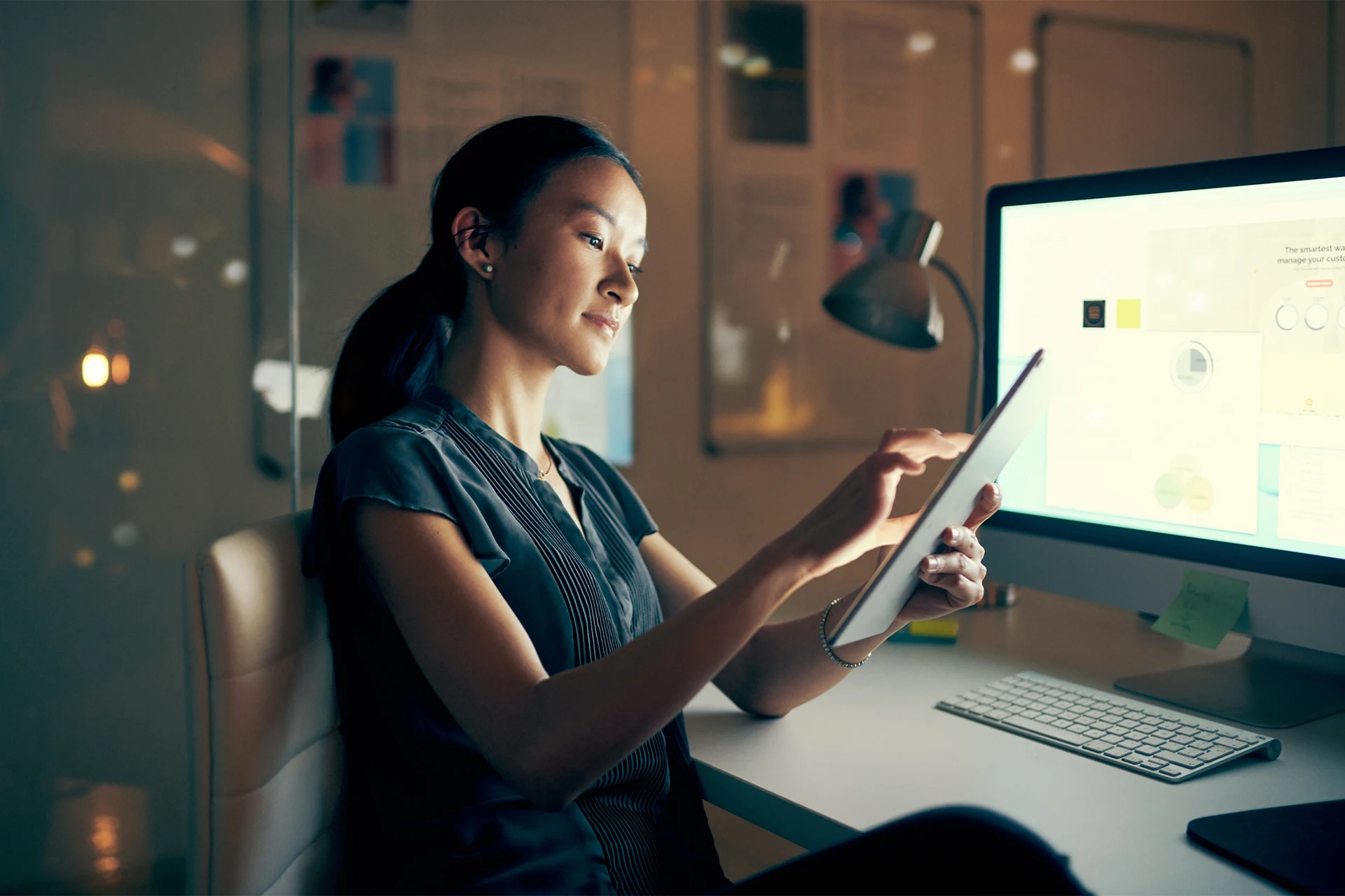 Professional using a tablet while working at a computer in a modern office setting