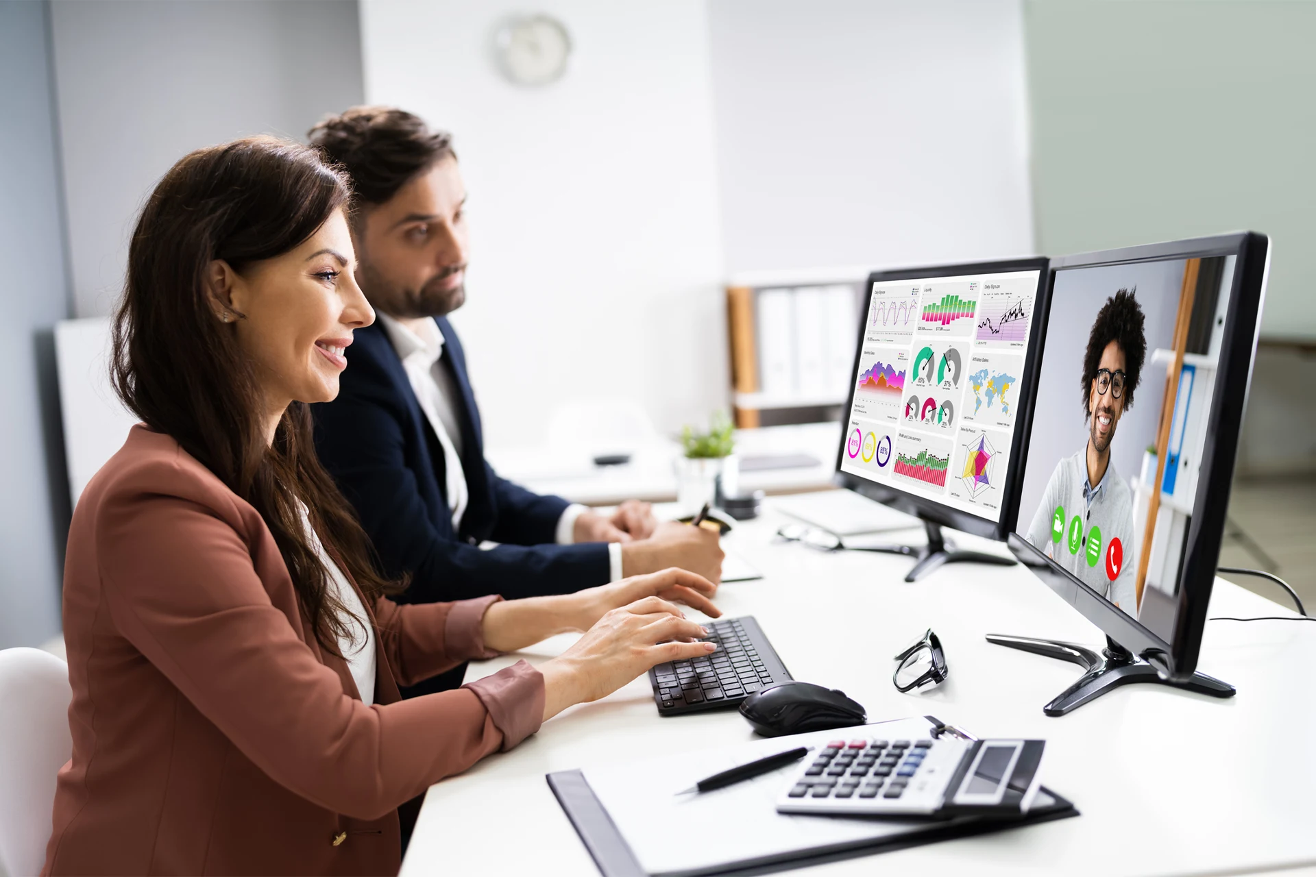 Two professionals engaged in a video conference meeting with data on screens