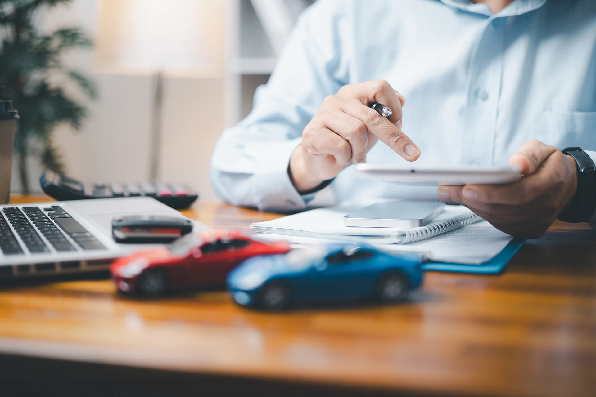 Person using a tablet at a desk with toy cars and a laptop present.