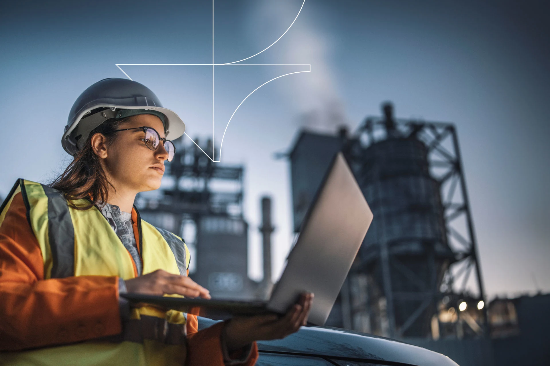 Worker in safety gear using a laptop near an industrial facility