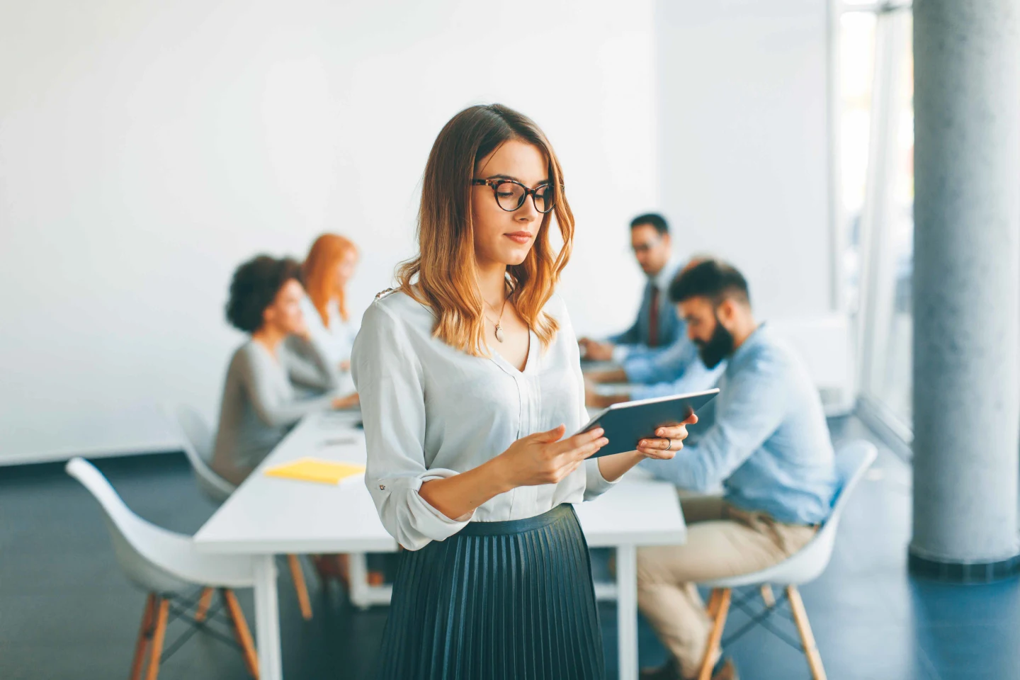 Professional holding a tablet while others collaborate in a meeting.