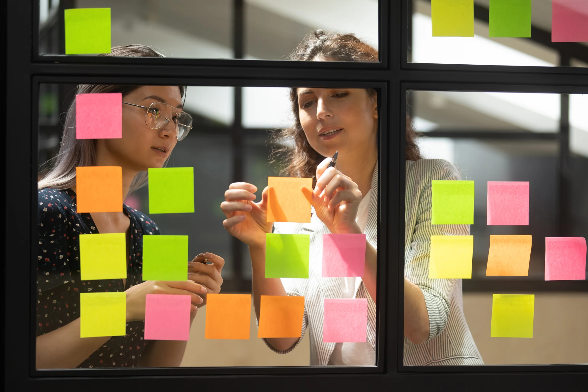 Two professionals collaborating with sticky notes on a glass board