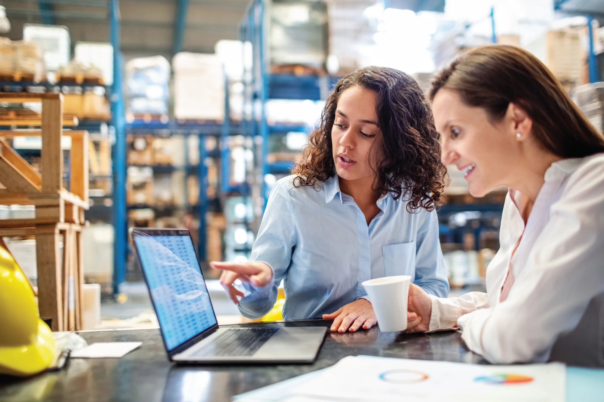 Two professionals discussing data insights on a laptop in a warehouse