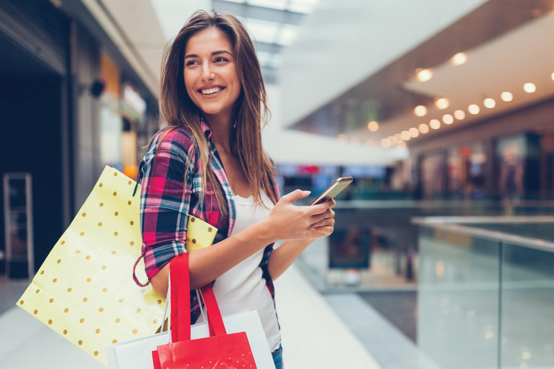 Woman using a smartphone while holding shopping bags in a mall