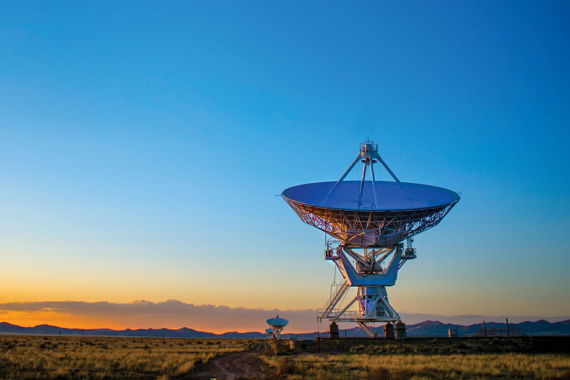 Satellite dish for broadcasting communications in a field at sunset