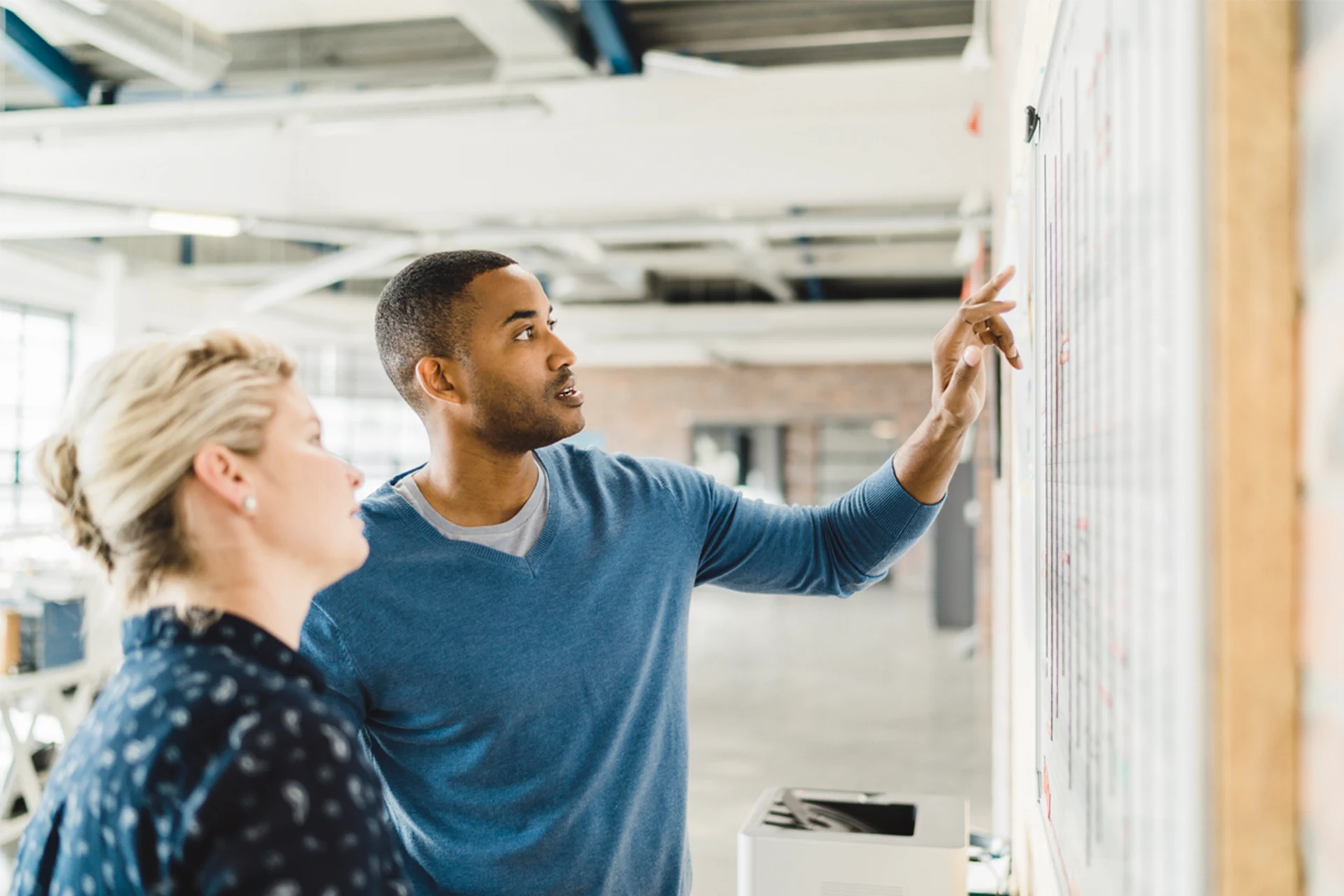 Two professionals discussing a project beside a whiteboard in an office.