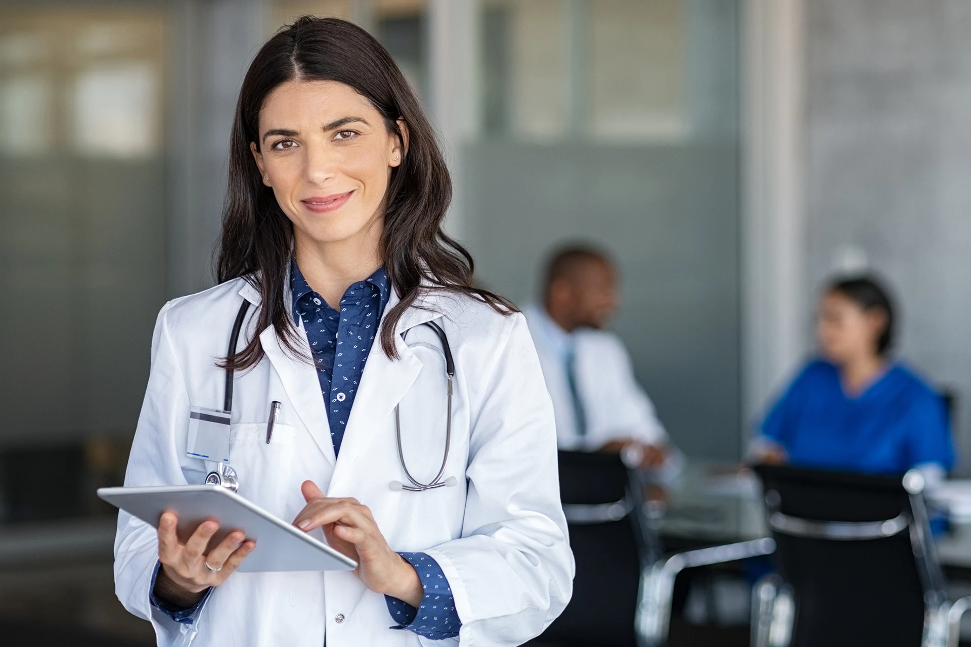 Healthcare professional holding a tablet, with colleagues in the background.