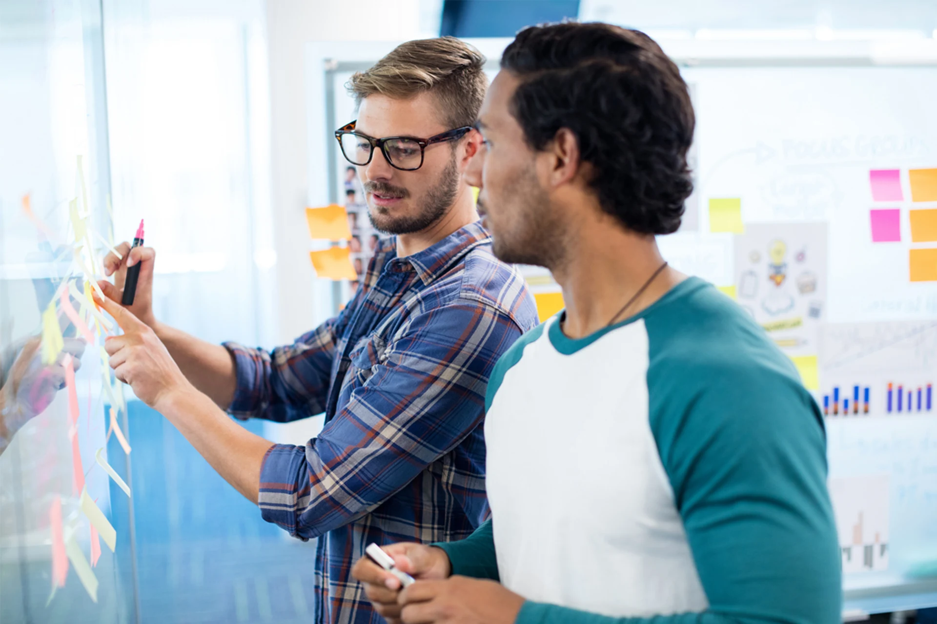 Two professionals collaborating on a whiteboard with sticky notes.