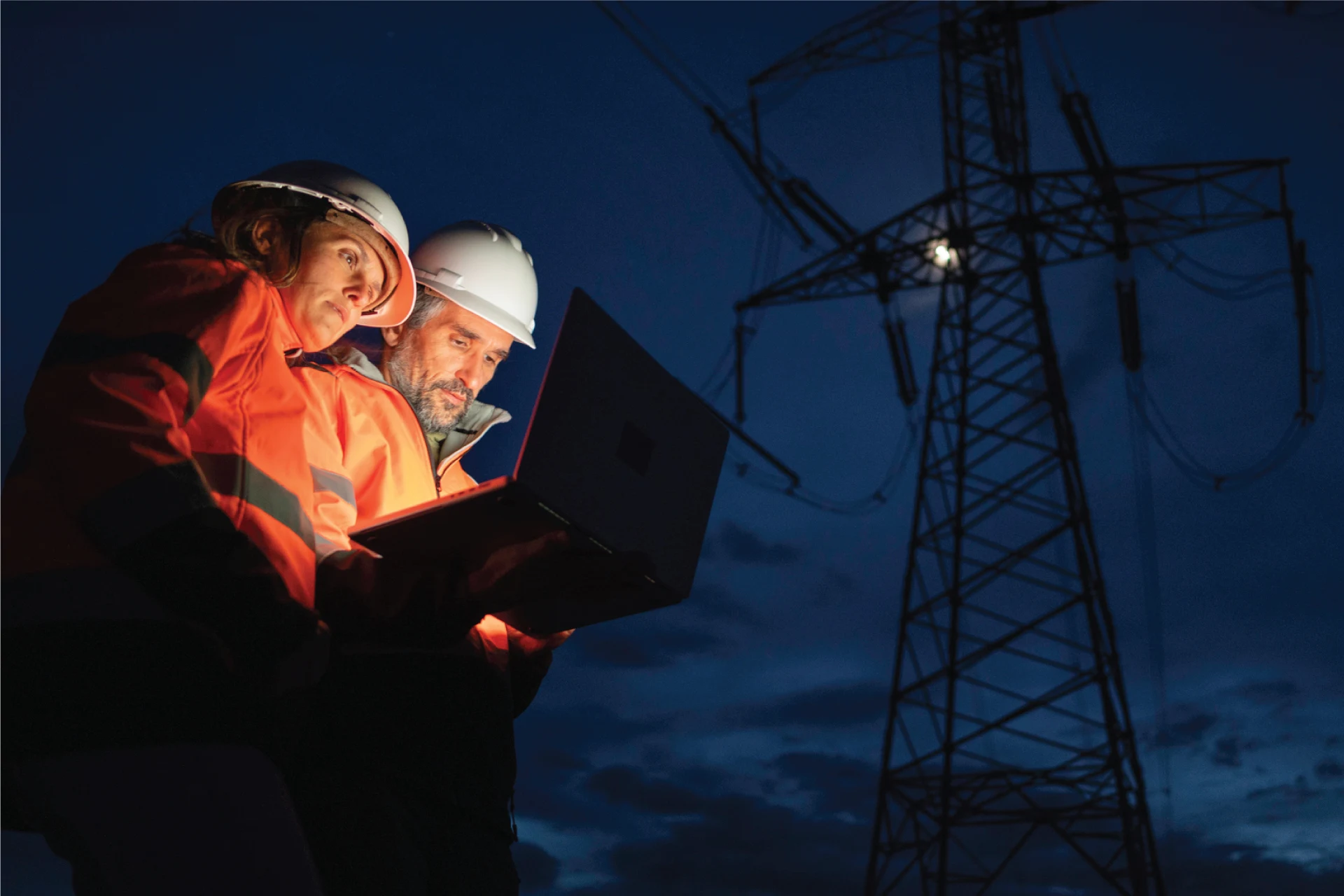 Two professionals analyzing data on a laptop near a power line