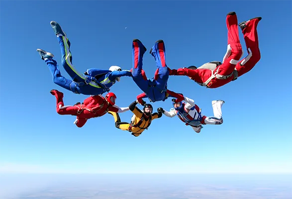Six skydivers performing coordinated formation jump against clear blue sky