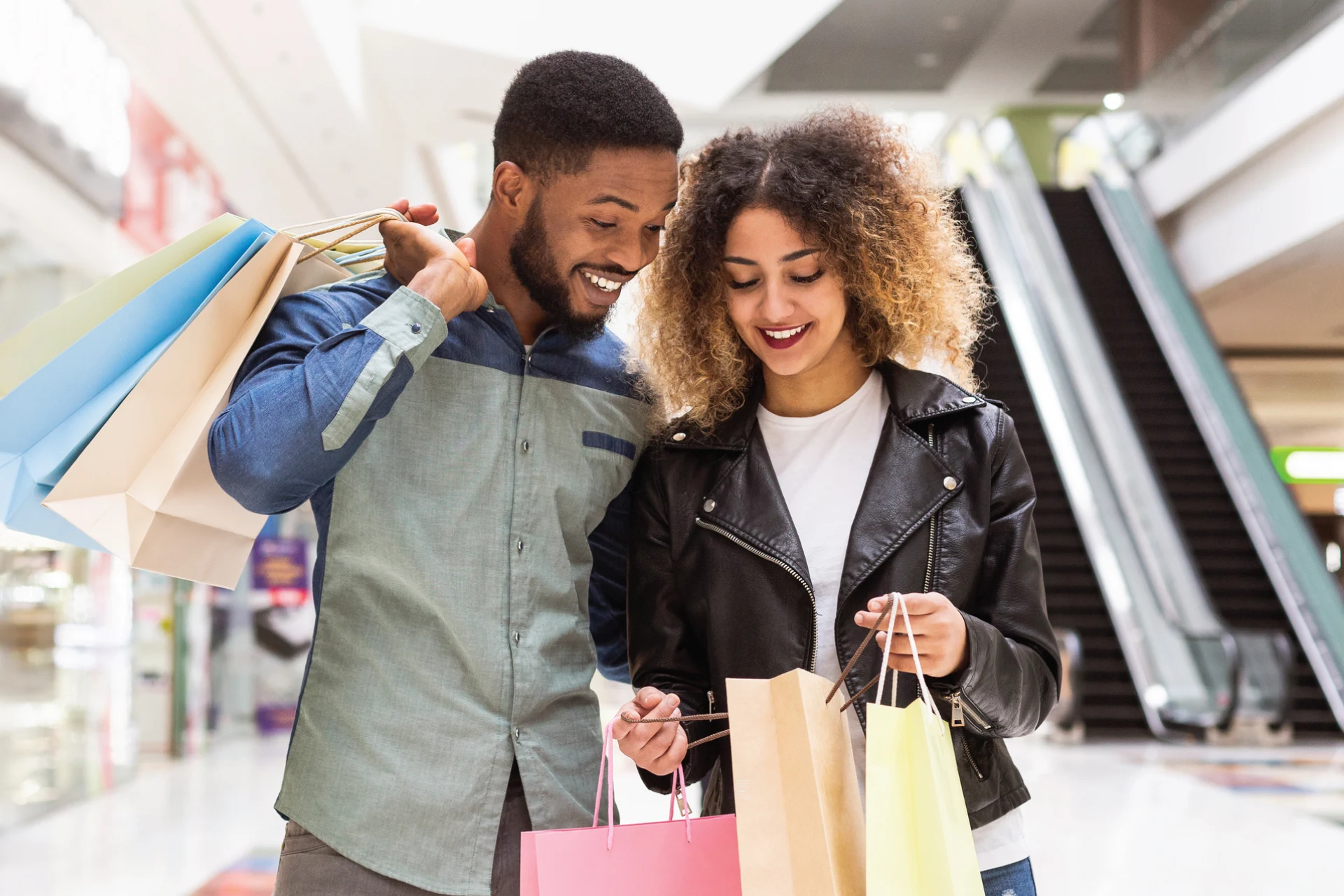 Two shoppers in a mall holding shopping bags after a purchase.