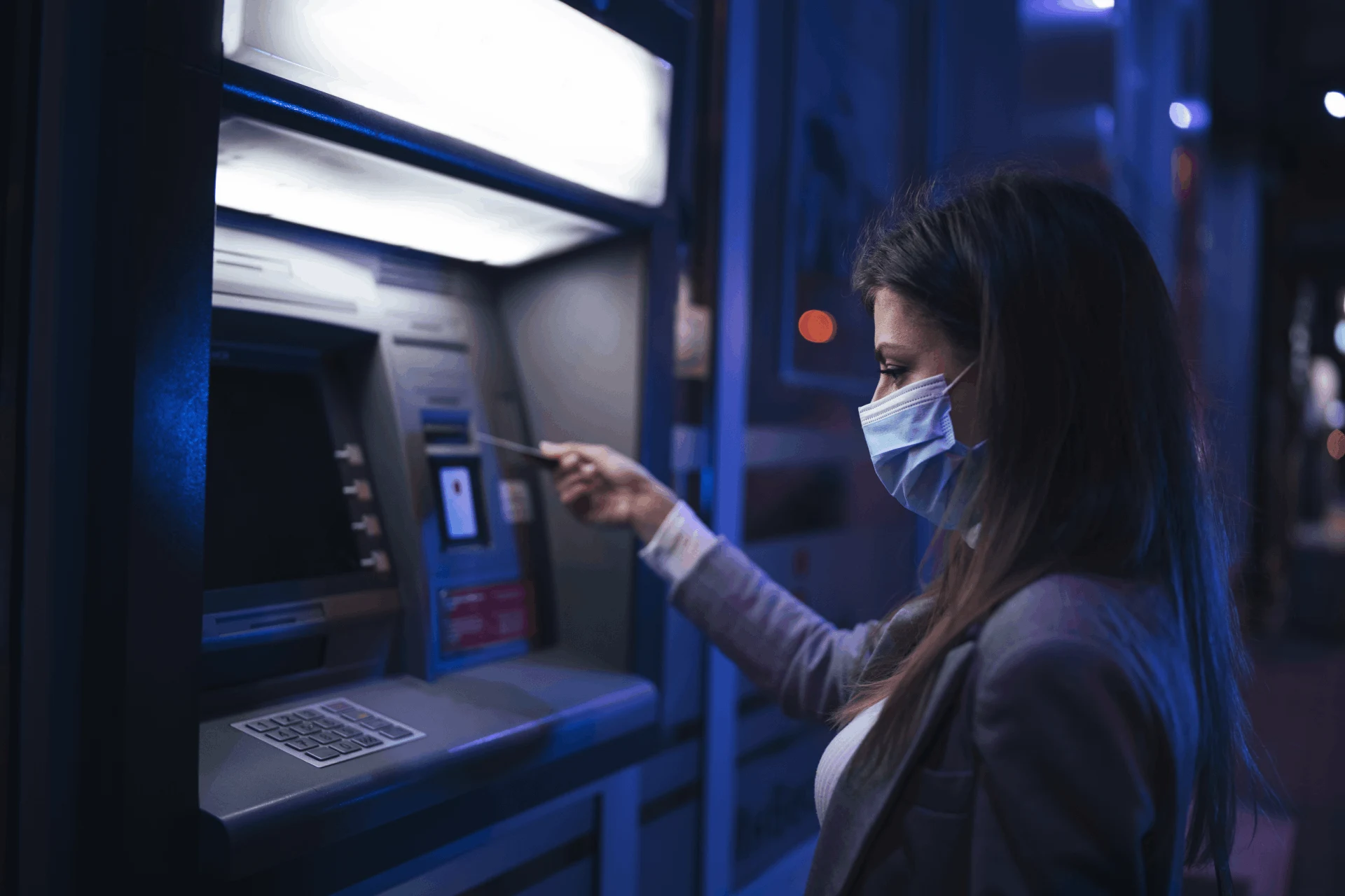 Woman using an ATM at night in a cashless economy context