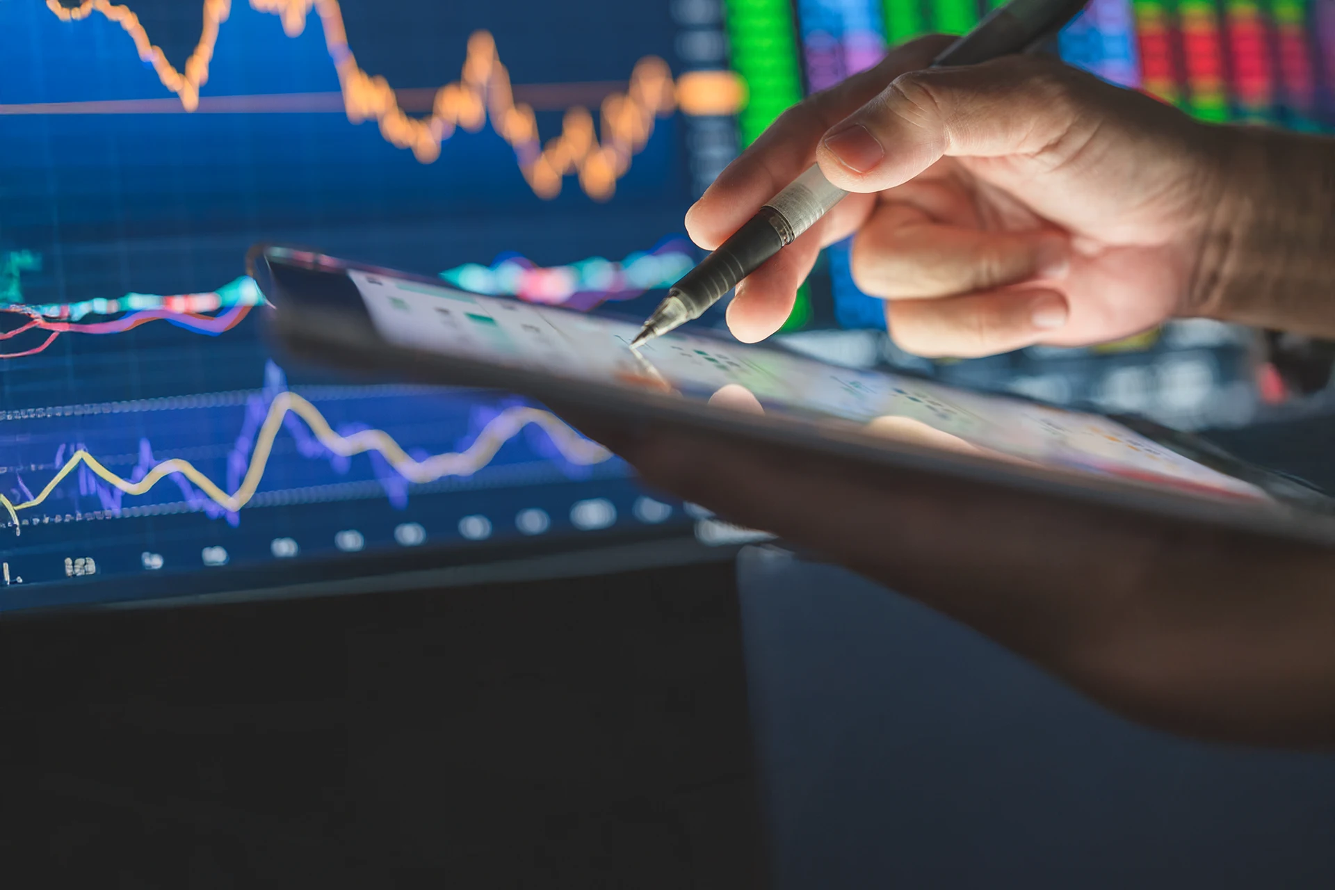 Person analyzing financial data on a tablet with market graphs in view.