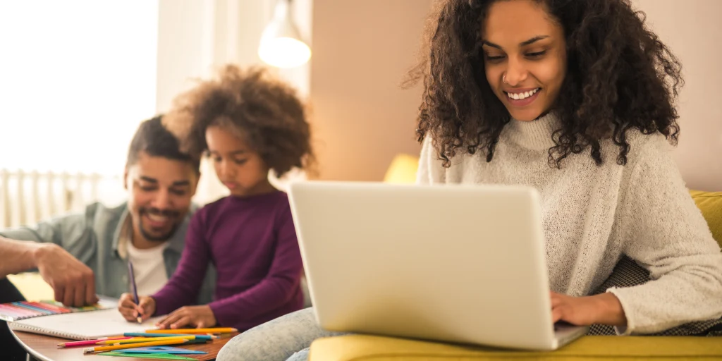 Mother working on laptop while children draw for Claimatic partnership