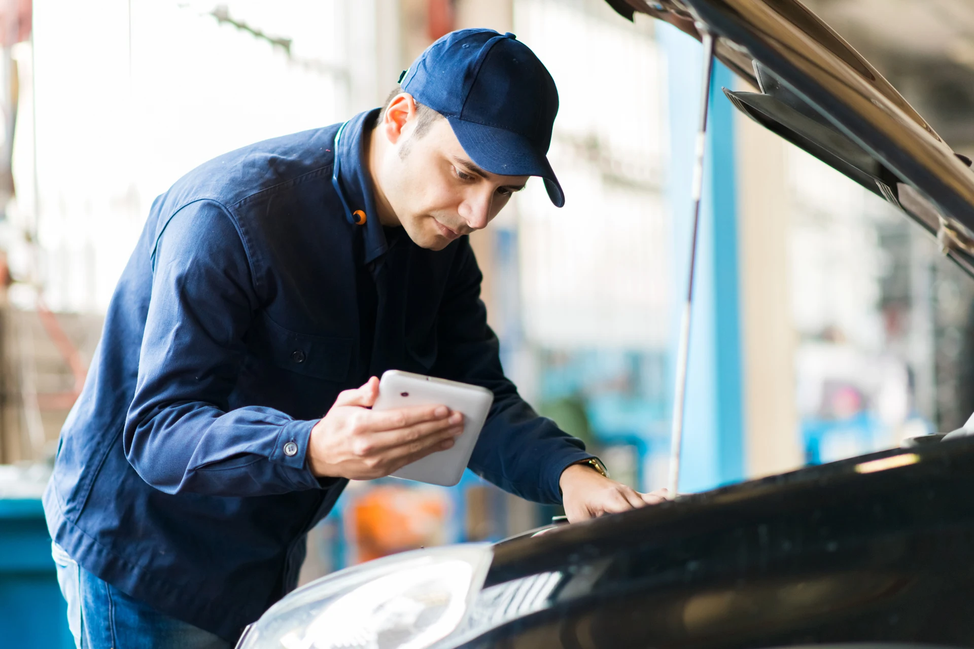 Technician using a tablet while inspecting a vehicle in a workshop.