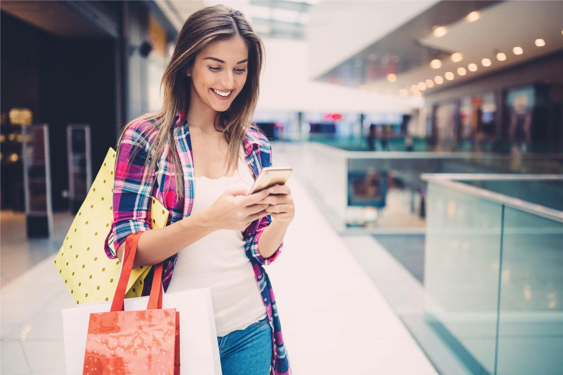 Young woman shopping with bags and using her smartphone in a mall.
