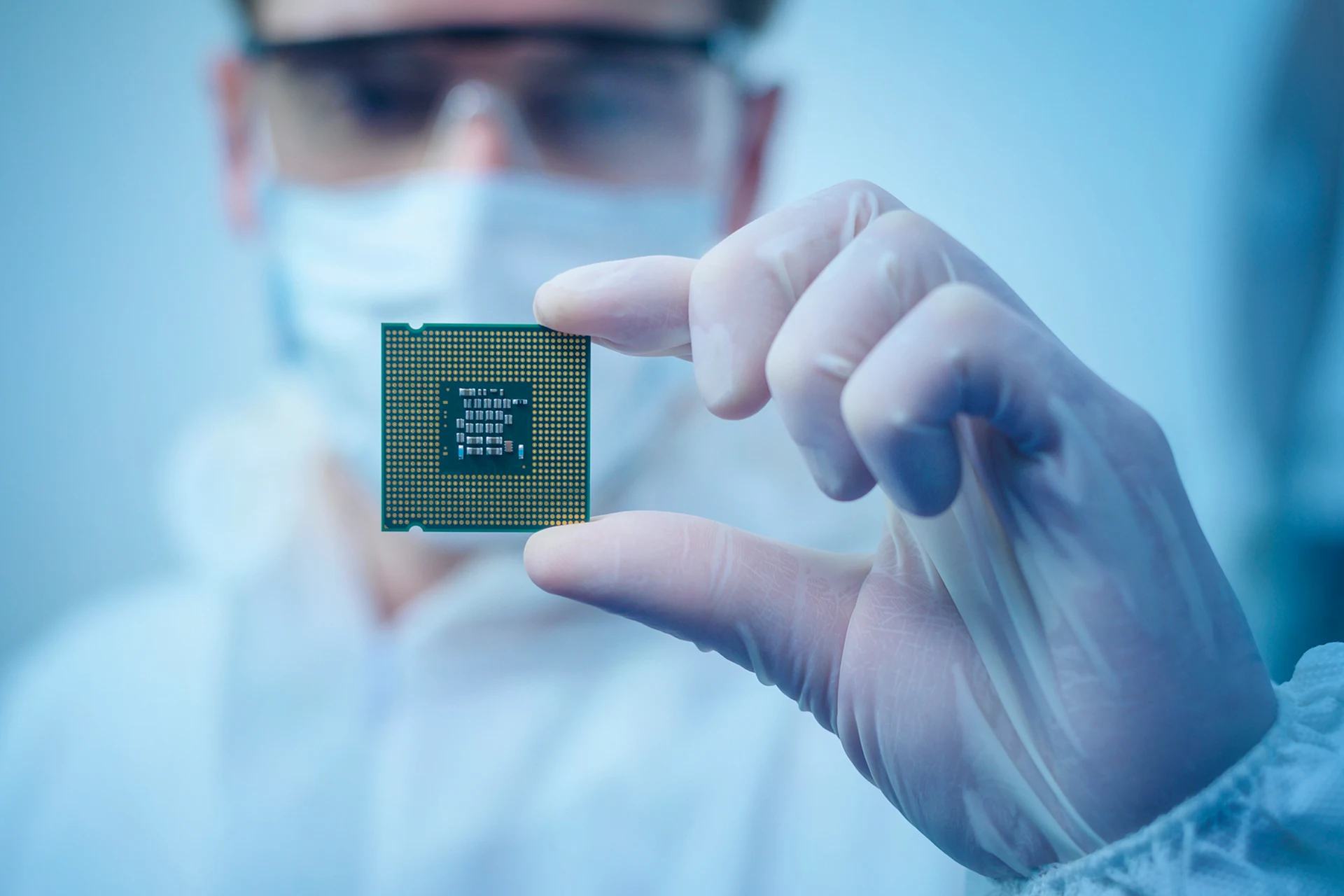 Person in protective gear holding a semiconductor chip for inspection
