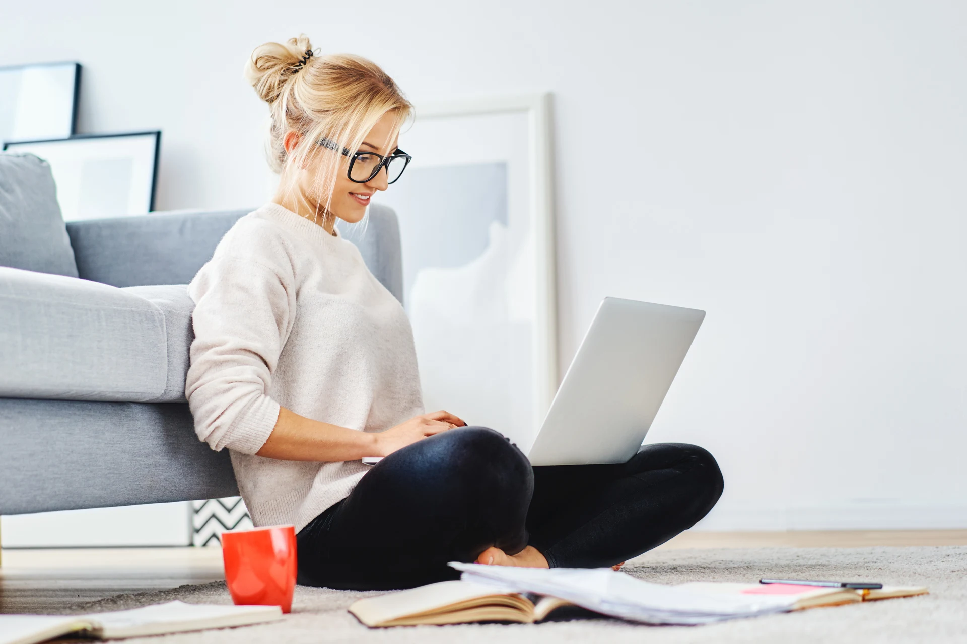 Person using a laptop on the floor surrounded by books and a red cup