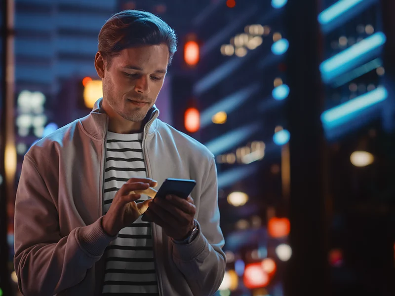 Person using smartphone in a city at night, symbolizing modern application services