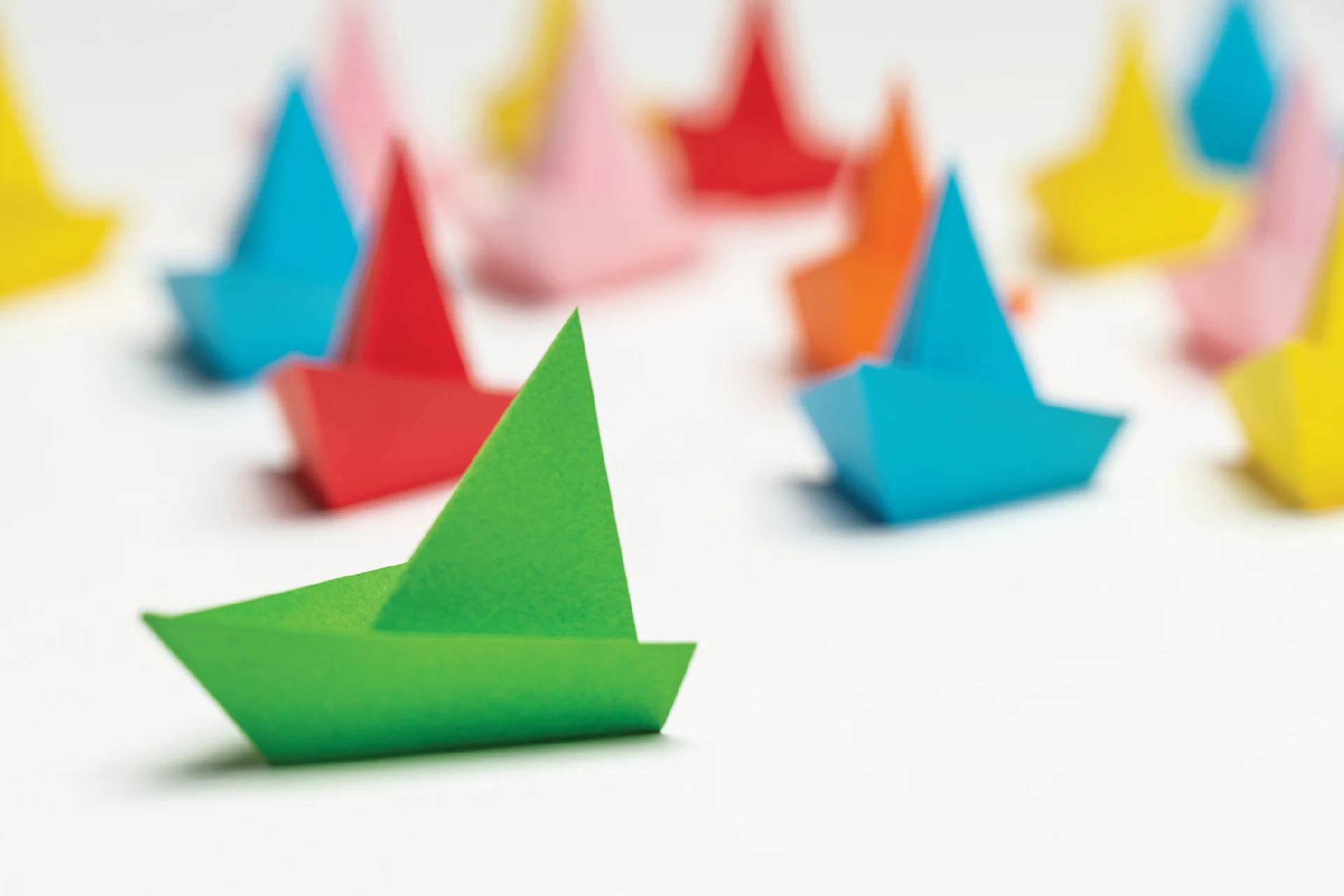 Green paper boat in focus among multiple colorful paper boats