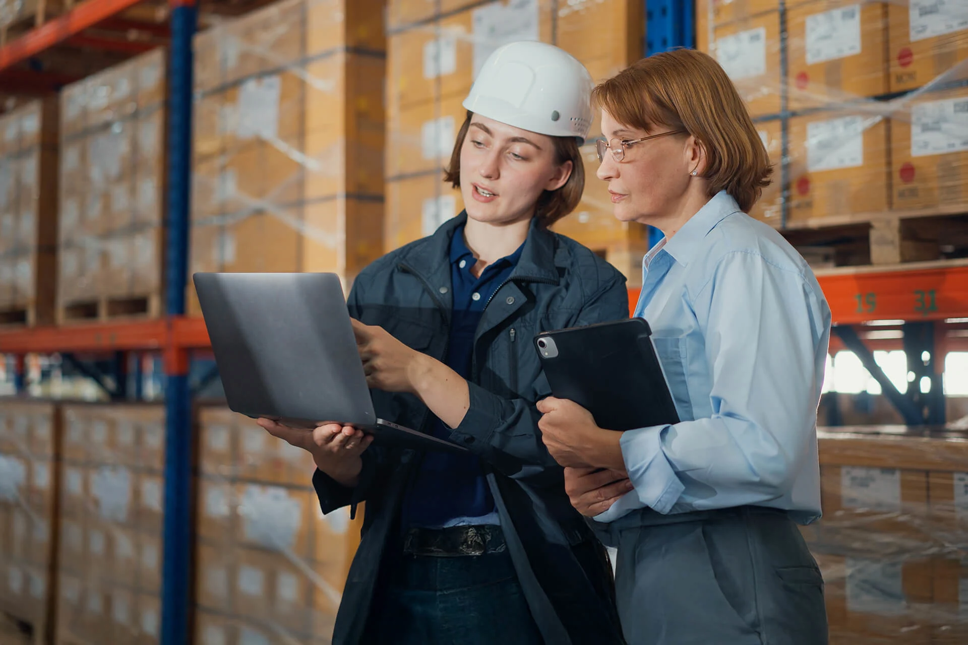 Two women discussing supply chain management while using a laptop