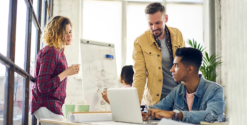 Business team collaborating around laptop screen in modern tech workspace