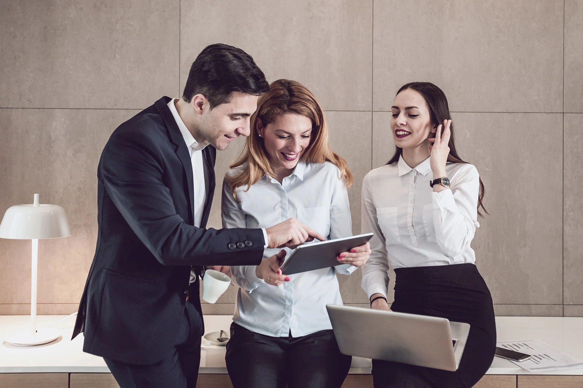 Three professionals collaborating on a tablet in a modern office setting.