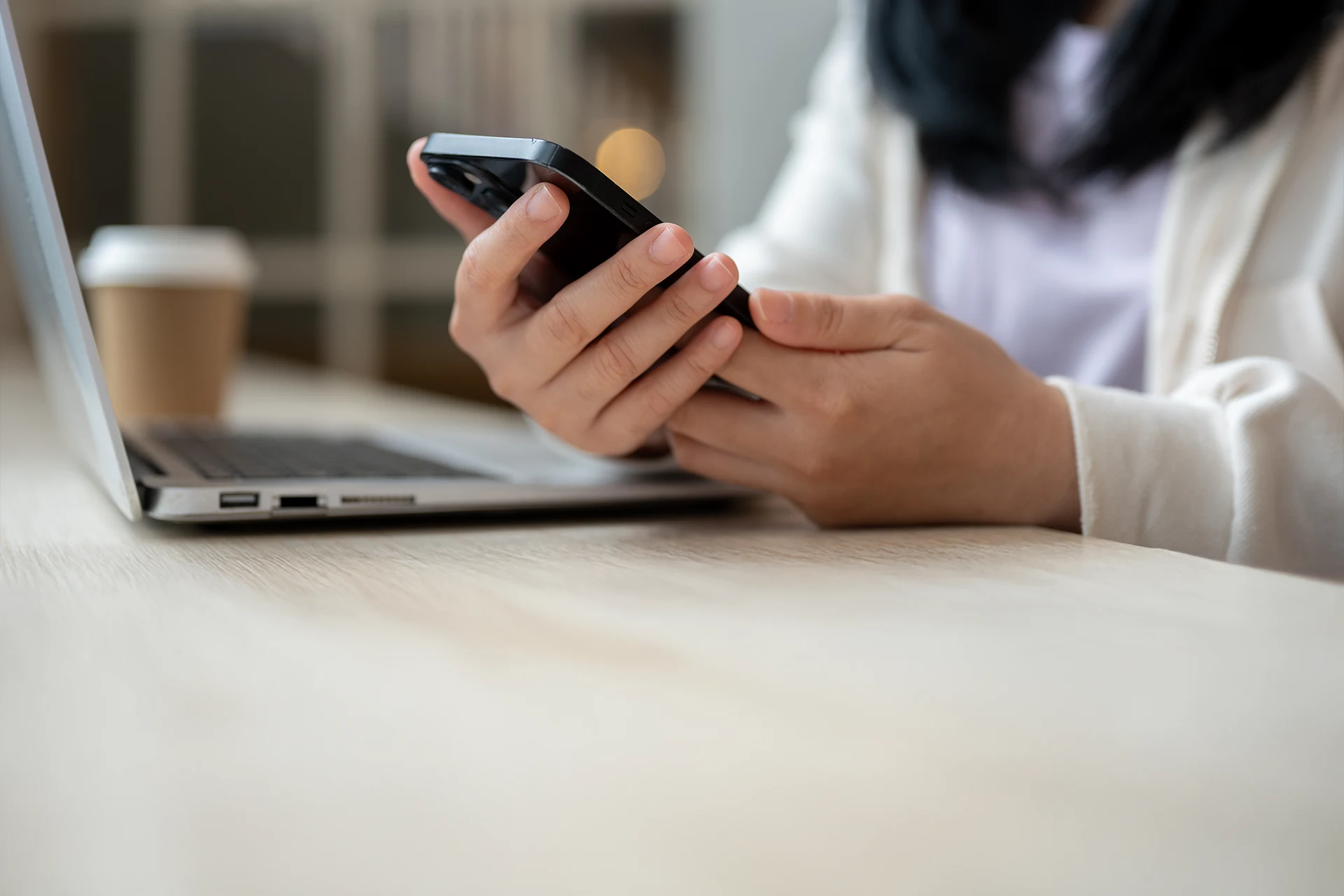 Person holding a smartphone while using a laptop in a workspace.